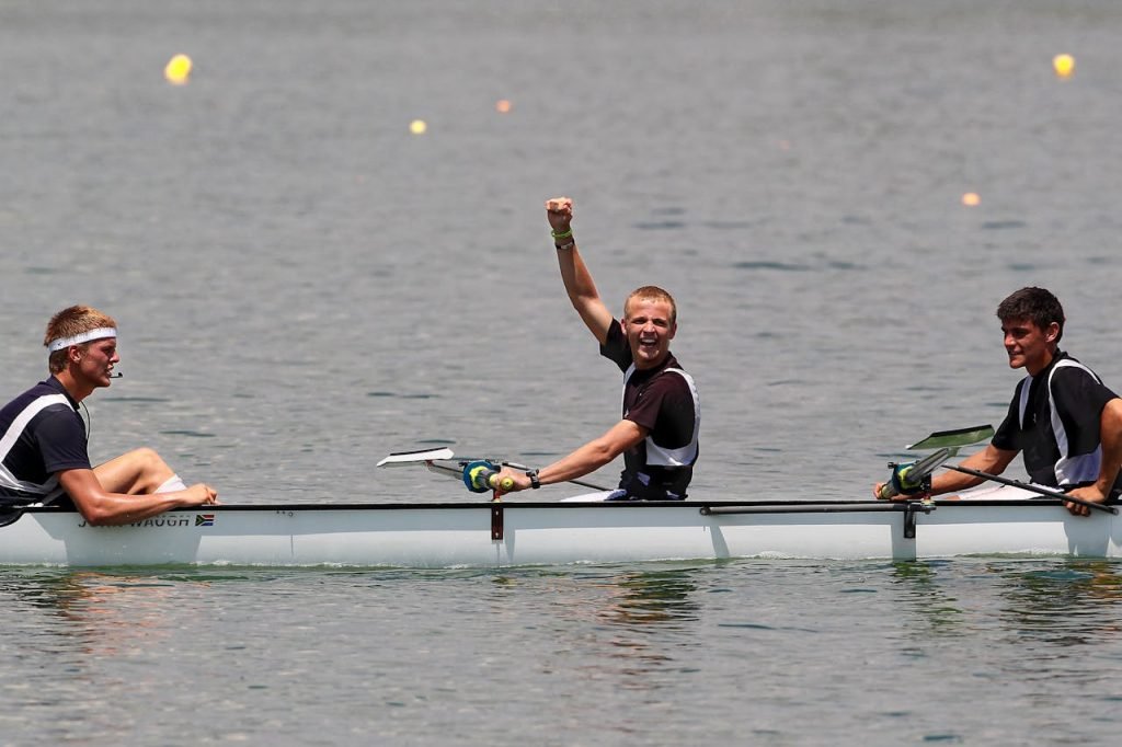 Three male rowers celebrating a win while competing on a calm lake.