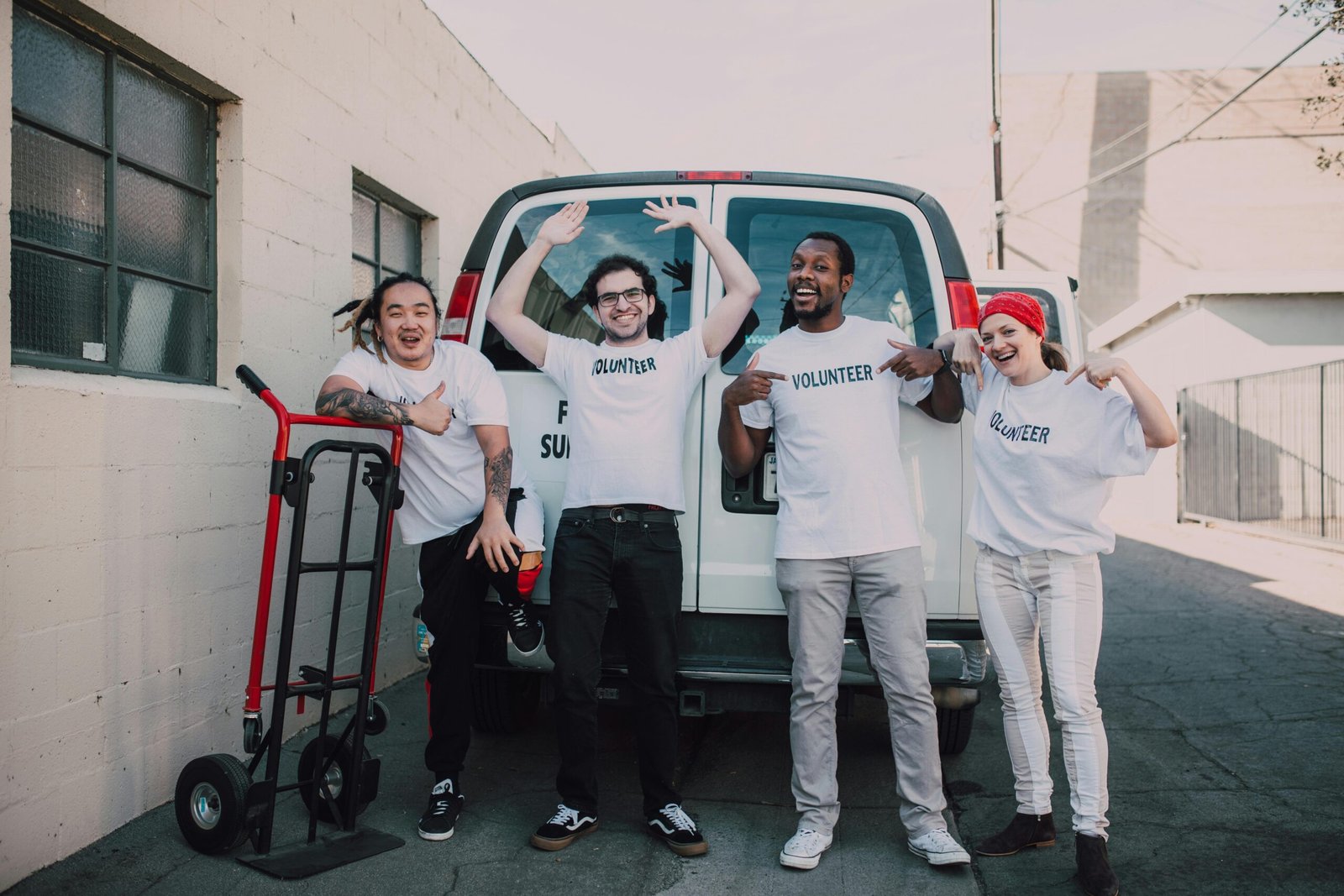 A diverse group of cheerful volunteers posing in front of a van, ready to help the community.