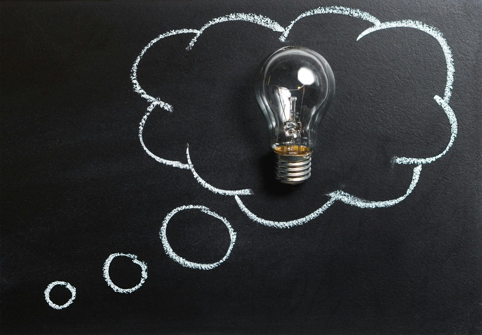 Light bulb laying on chalkboard with drawn thought bubble, symbolizing creative ideas.